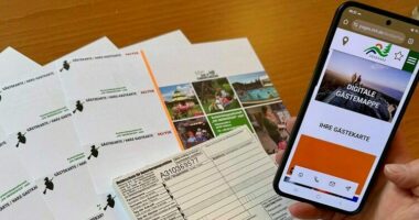 Handy, das die digitale Gästekarte auf demm Handy zeigt, alte Papiergästekarten ligen im Hintergrund