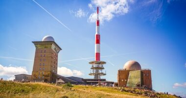 Gipfel mit Häusern und Sendeturm des Brocken im Harz-Nationalpark im Hintergrund blauer Himmel