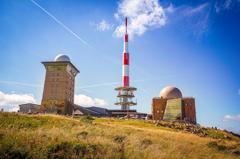Gipfel mit Häusern und Sendeturm des Brocken im Harz-Nationalpark im Hintergrund blauer Himmel